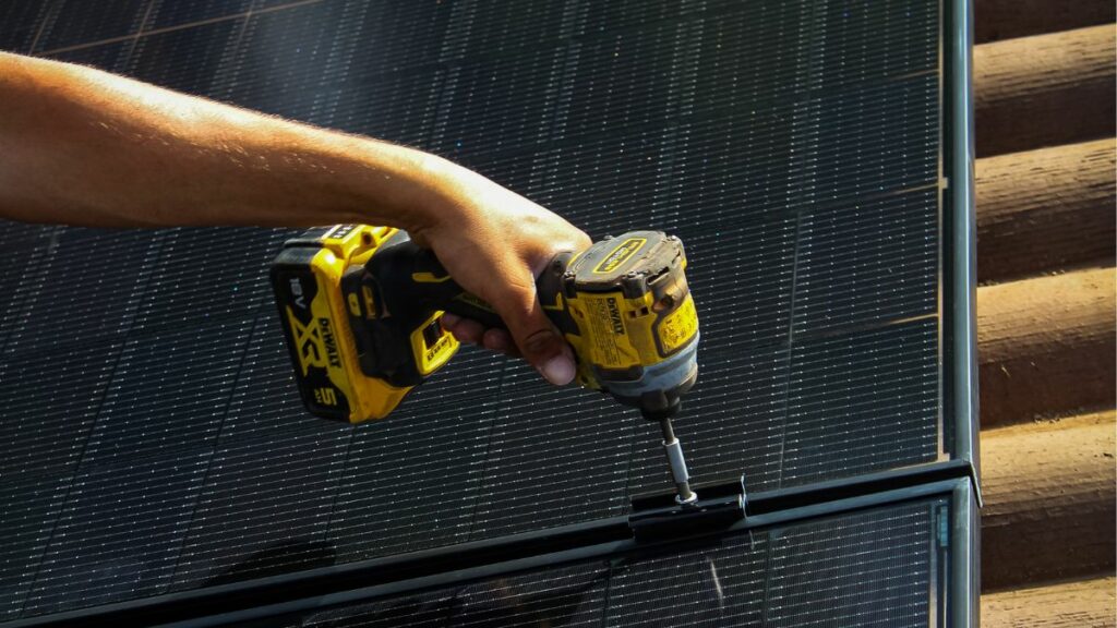 Main d'un installateur tenant une perceuse au dessus d'un panneau photovoltaïque